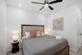 Bedroom with a wooden-framed bed, gray comforter, and orange throw pillows; two nightstands with lamps flank the bed