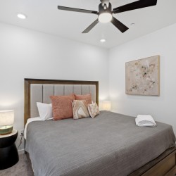 Bedroom with a wooden-framed bed, gray comforter, and orange throw pillows; two nightstands with lamps flank the bed