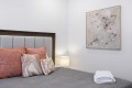 Bedroom scene with a gray upholstered bed, rust-orange and patterned pillows, and a folded white towel on a gray coverlet.