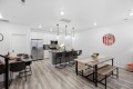 Open-concept kitchen and dining area with white cabinets, stainless fridge, island with black stools, and a wooden dining table on the right.