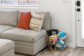 Grey fabric sofa with an orange patterned throw pillow and a beige striped pillow, next to a wicker basket filled with colorful sports balls by the door.