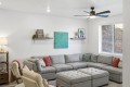 Bright living room with a gray sectional sofa, tufted ottoman, and decorative teal art on the wall above two floating shelves.