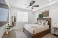 Wood bed with beige bedding and patterned throw pillows in a bright modern bedroom, ceiling fan above.