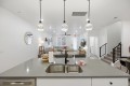 Open-concept kitchen and living area with a gray island, double sink, and pendant globe lights overlooking a cozy seating space.