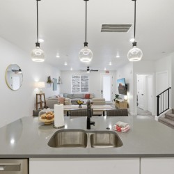 Open-concept kitchen and living area with a gray island, double sink, and pendant globe lights overlooking a cozy seating space.