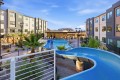 Outdoor pool area at a modern apartment complex, featuring a bright blue winding water slide, lounge chairs, and tropical landscaping under a clear sky.