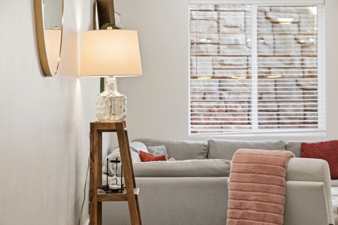 Living room scene with a glass-lit lamp on a wooden ladder-style side table beside a gray sofa and pink throw blanket on the armrest.
