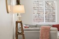 Living room scene with a glass-lit lamp on a wooden ladder-style side table beside a gray sofa and pink throw blanket on the armrest.
