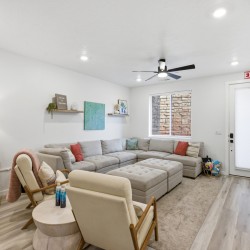 Cozy living room with a light gray sectional sofa, two beige armchairs, round ottoman, and a neutral rug.