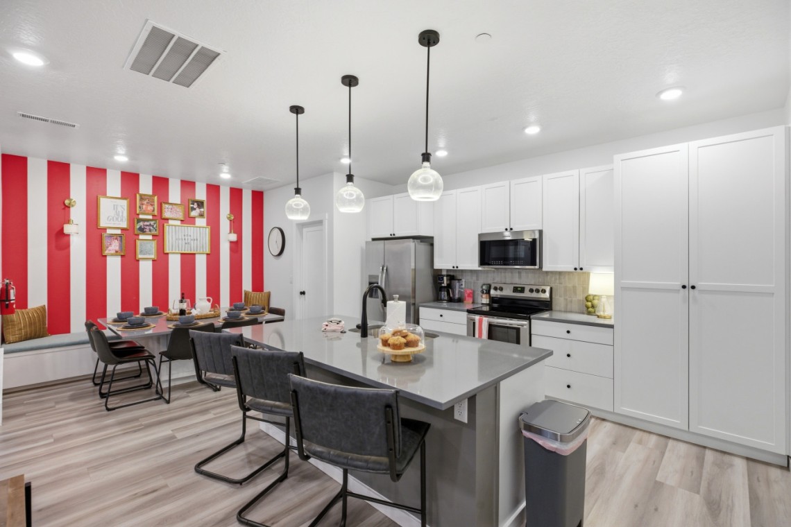 Modern kitchen and dining area with white cabinets, gray island, stainless appliances, and a bold red-and-white striped accent wall
