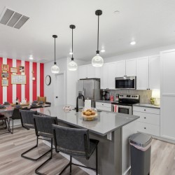 Modern kitchen and dining area with white cabinets, gray island, stainless appliances, and a bold red-and-white striped accent wall