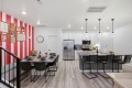 Open-concept kitchen and dining area with a pink striped accent wall, framed art, and a long dining table set for eight beside a white-cabinet kitchen and island with bar stools.