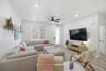 Bright living room with a large light-gray sectional sofa, matching ottoman, and pastel throw pillows facing a wall-mounted flat-screen TV.