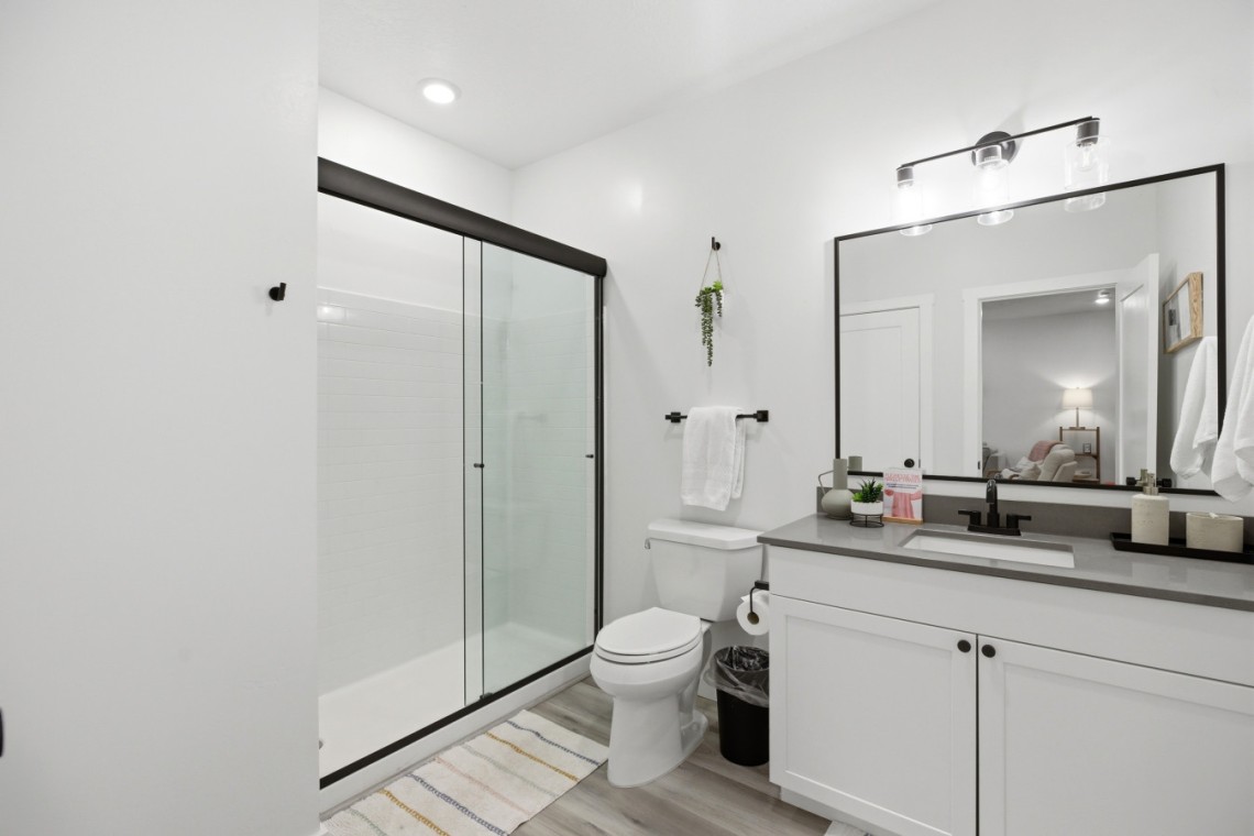 Bright, modern bathroom with a glass-framed shower, white subway tiles, and a large rectangular mirror above a gray countertop vanity.