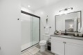 Bright, modern bathroom with a glass-framed shower, white subway tiles, and a large rectangular mirror above a gray countertop vanity.