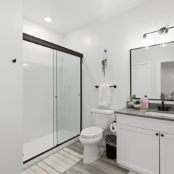 Bright, modern bathroom with a glass-framed shower, white subway tiles, and a large rectangular mirror above a gray countertop vanity.