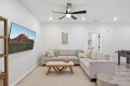 L-shaped beige sofa with decorative pillows facing a wall-mounted flat-screen TV showing a canyon landscape, in a bright living room.