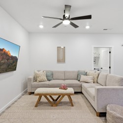 L-shaped beige sofa with decorative pillows facing a wall-mounted flat-screen TV showing a canyon landscape, in a bright living room.