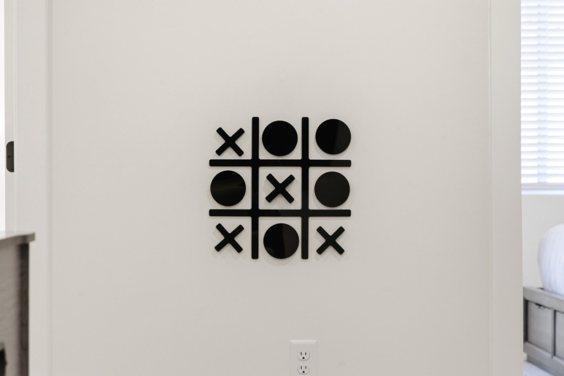 Decorative wall art of a tic-tac-toe grid with black X and O shapes on a white wall.