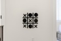 Decorative wall art of a tic-tac-toe grid with black X and O shapes on a white wall.
