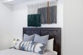 Bedroom with a dark wood headboard, layered pillows, and a large gradient textile wall hanging above the bed.