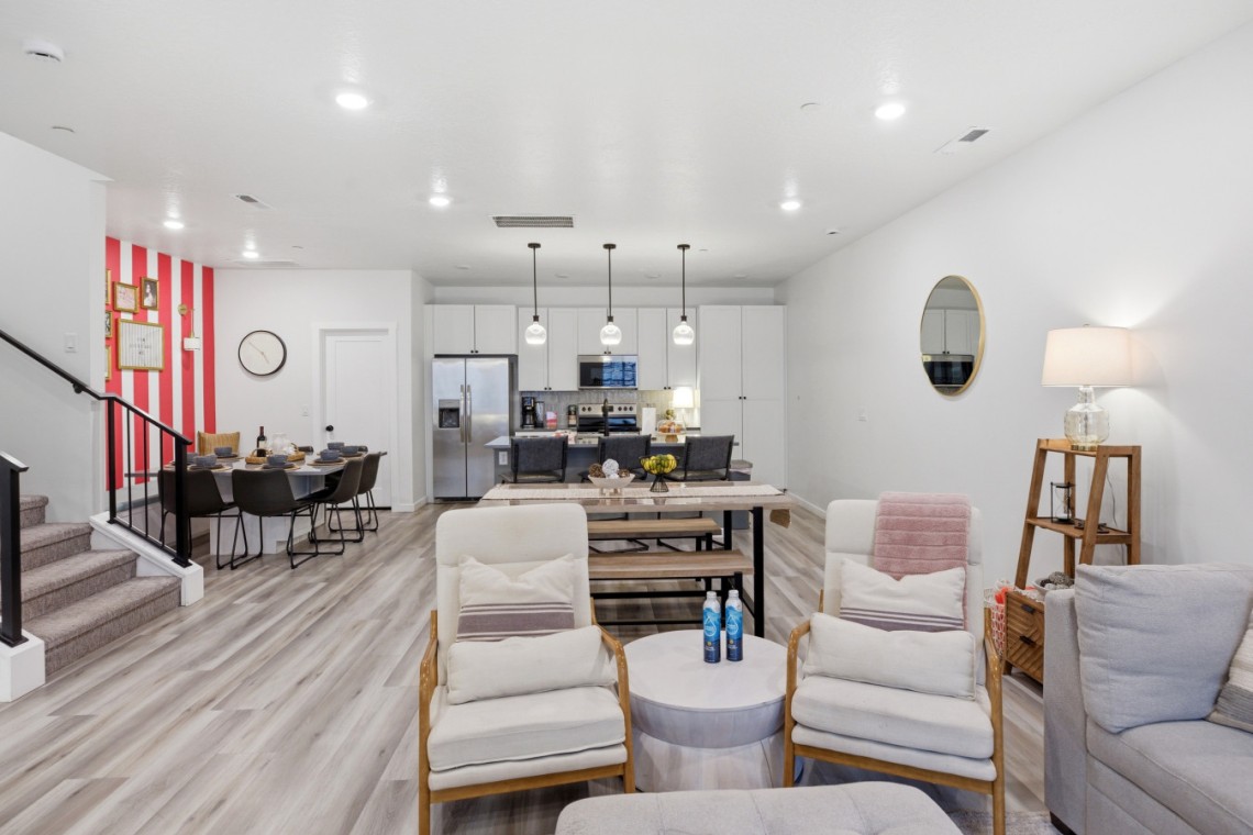 Open-concept living space with a bright kitchen, white cabinets, stainless-steel appliances, and pendant lights over an island.