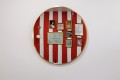 Round wall mirror reflecting a red-and-white striped gallery wall with multiple framed pictures and a small wall lamp on the left.