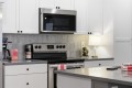 Modern kitchen with stainless steel microwave above a range, white cabinets, and a gray tiled backsplash.