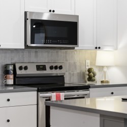 Modern kitchen with stainless steel microwave above a range, white cabinets, and a gray tiled backsplash.