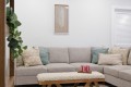 Beige sectional sofa with multiple decorative pillows in a bright living room; a wooden coffee table with a tray of pink drinks sits in front.