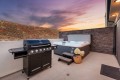 Patio at sunset with a black gas grill and a large hot tub against a stone wall.