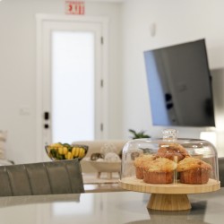 Muffins under a glass dome on a wooden cake stand atop a kitchen counter, with a paper towel roll nearby.