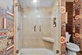 Glass-front walk-in shower with beige tile, chrome fixtures, and a built-in bench; Wild West patterned wallpaper surrounds a toilet on the right.