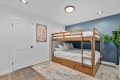 Wooden bunk bed with white bedding against a blue accent wall in a bright kids' room, with a potted plant and rug nearby.