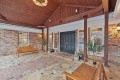 Covered brick entryway with dark double doors, wooden beams, and potted plants, welcoming visitors to a home.
