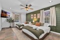 Two twin beds with olive-green throws and orange pillows in a bright bedroom with a green accent wall and framed art above.