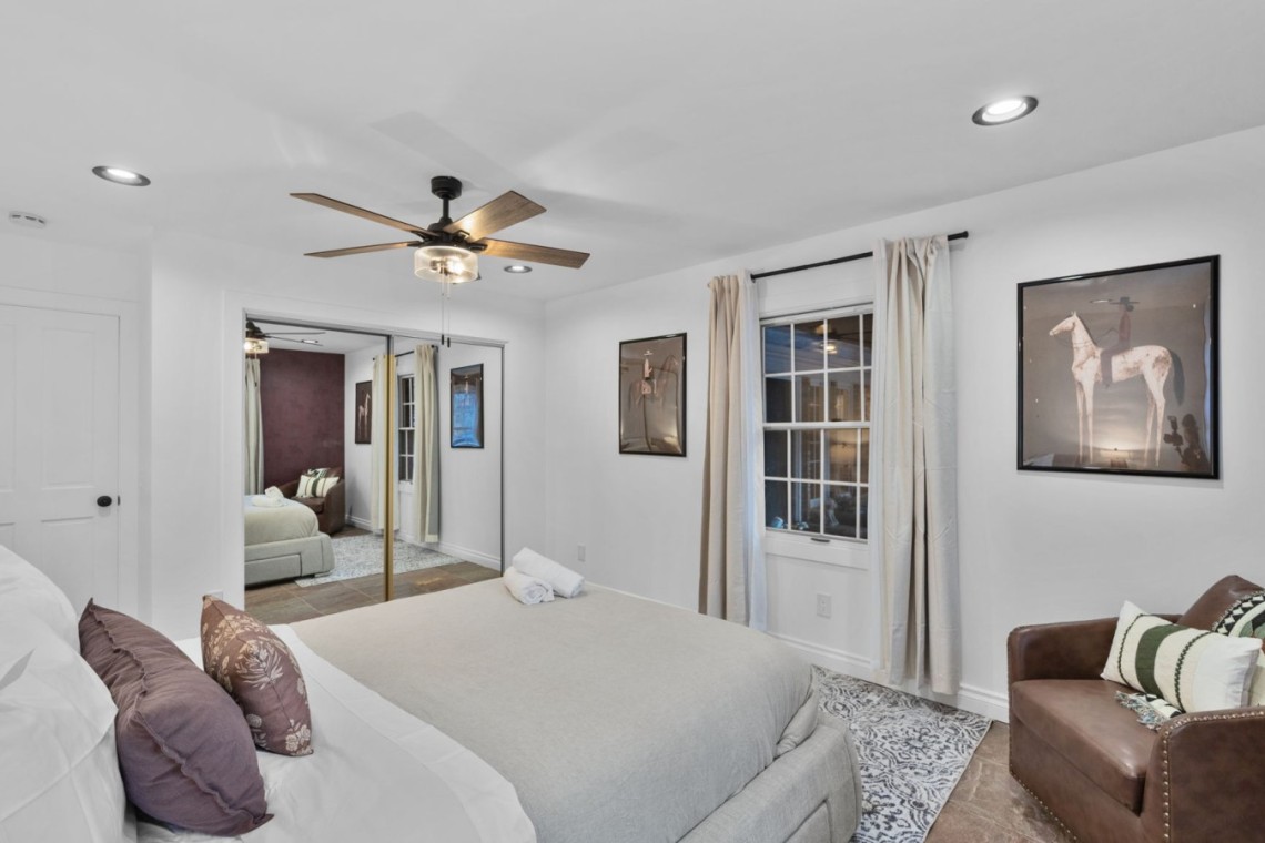 Bright, modern bedroom with a large bed, neutral bedding, and a brown leather chair by the window; horse artwork on the wall.