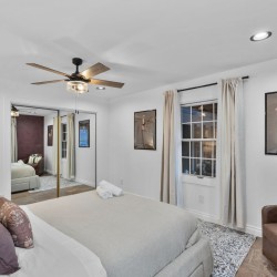 Bright, modern bedroom with a large bed, neutral bedding, and a brown leather chair by the window; horse artwork on the wall.