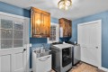 Laundry room with blue walls, wooden cabinets, a stainless sink, a front-load washer and a matching dryer, white doors nearby.