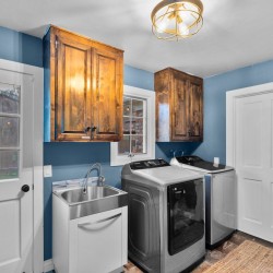 Laundry room with blue walls, wooden cabinets, a stainless sink, a front-load washer and a matching dryer, white doors nearby.