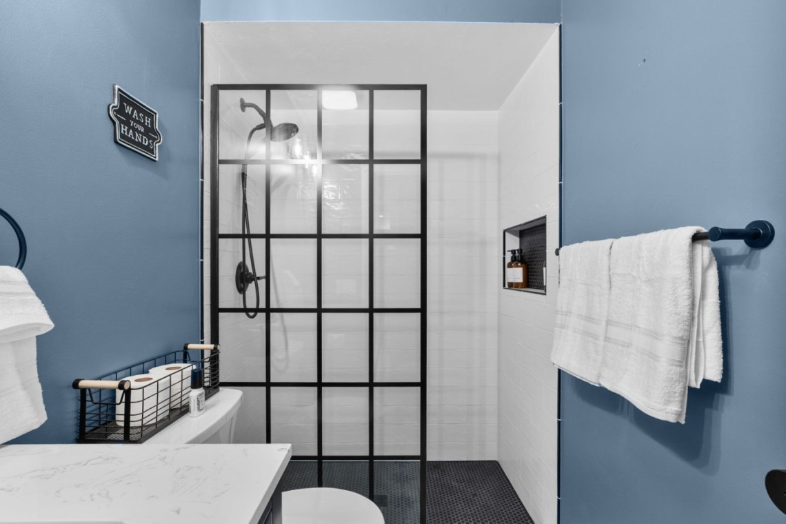 Blue bathroom with a black-framed glass-paned shower door, white subway tiles, and towels on dark blue walls.