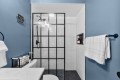 Blue bathroom with a black-framed glass-paned shower door, white subway tiles, and towels on dark blue walls.