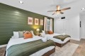 Bedroom with two twin beds, white linens, olive green shiplap wall, and a ceiling fan overhead.