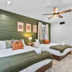 Bedroom with two twin beds, white linens, olive green shiplap wall, and a ceiling fan overhead.