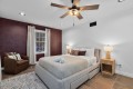 Modern bedroom with a gray upholstered bed, burgundy accent wall, window with light curtains, and two nightstands with lamps on either side of the bed.