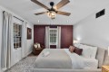 Bedroom with gray upholstered bed, white linens, and burgundy accent wall under a wooden ceiling fan.