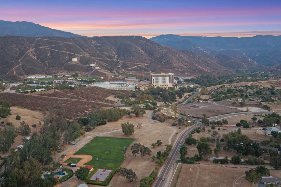 Aerial view of a valley town at sunset, with rugged hills in the background and a curved highway in the foreground.