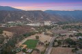 Aerial view of a valley town at sunset, with rugged hills in the background and a curved highway in the foreground.