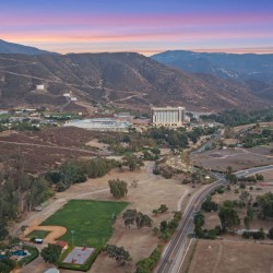 Aerial view of a valley town at sunset, with rugged hills in the background and a curved highway in the foreground.