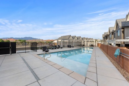 Outdoor pool area of a residential community with lounge chairs, white pergolas, and distant mountains in view.